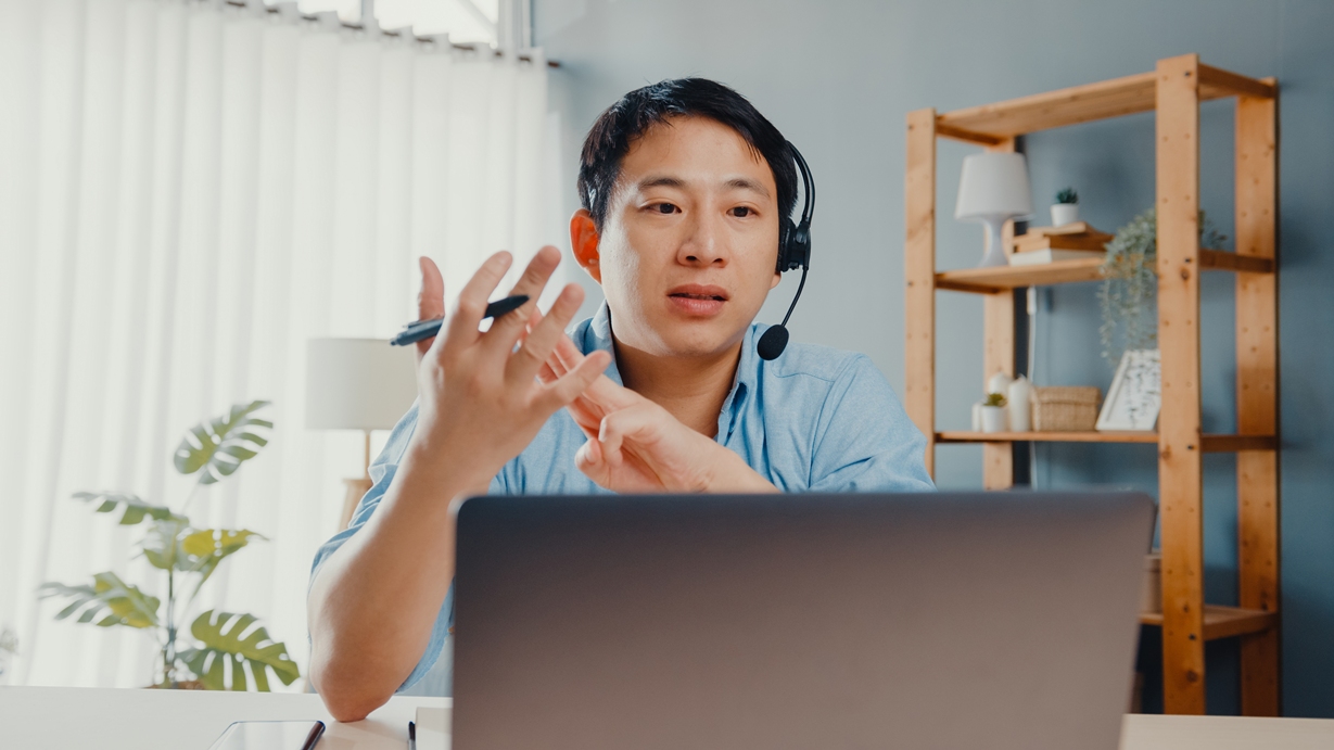 young-asia-businessman-wear-headphones-using-laptop-talk-colleagues-about-plan-video-call-while-work-from-home-living-room